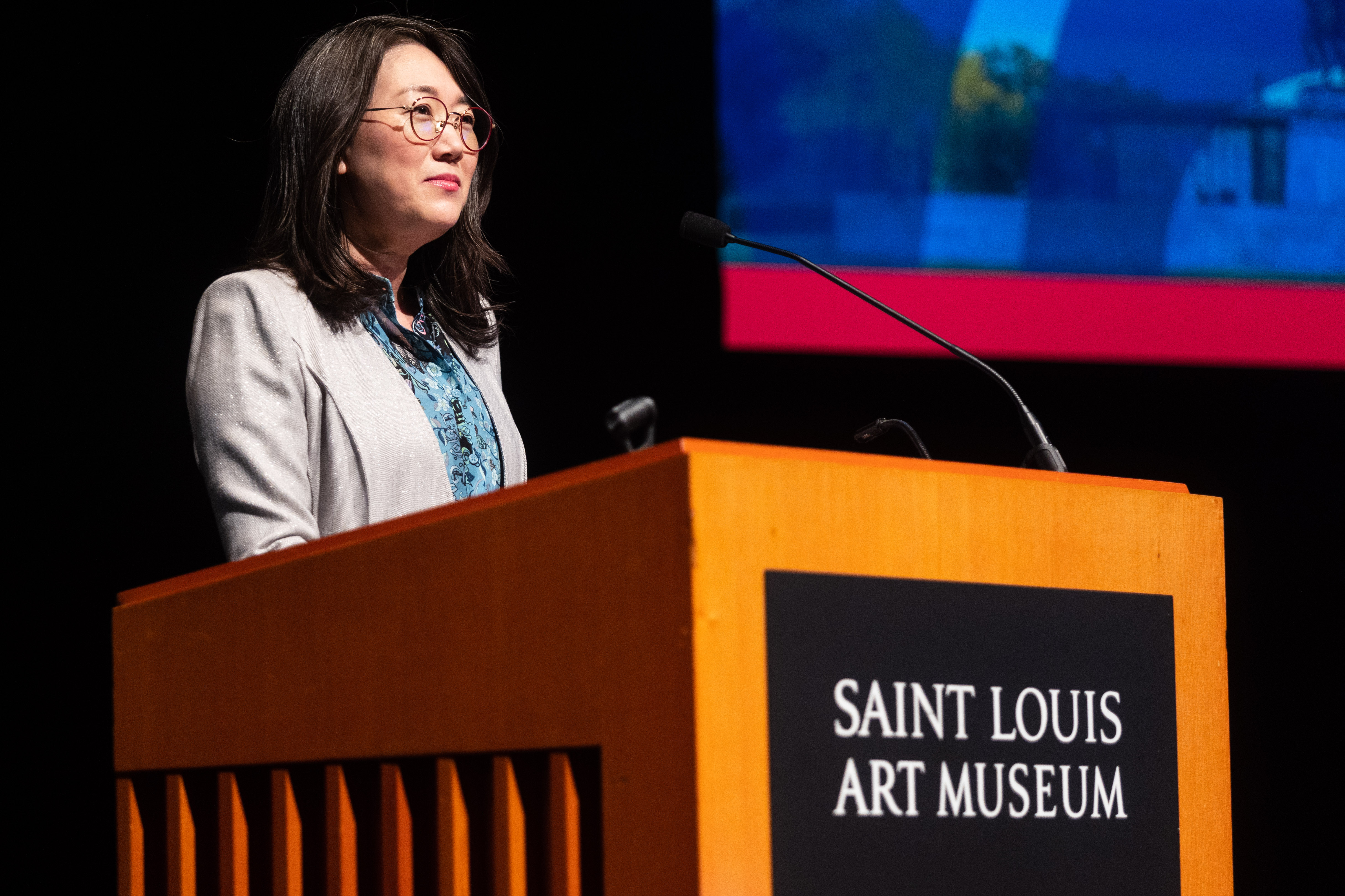 Min Jung Kim speaks to an audience on the stage at the Saint Louis Art Museum.