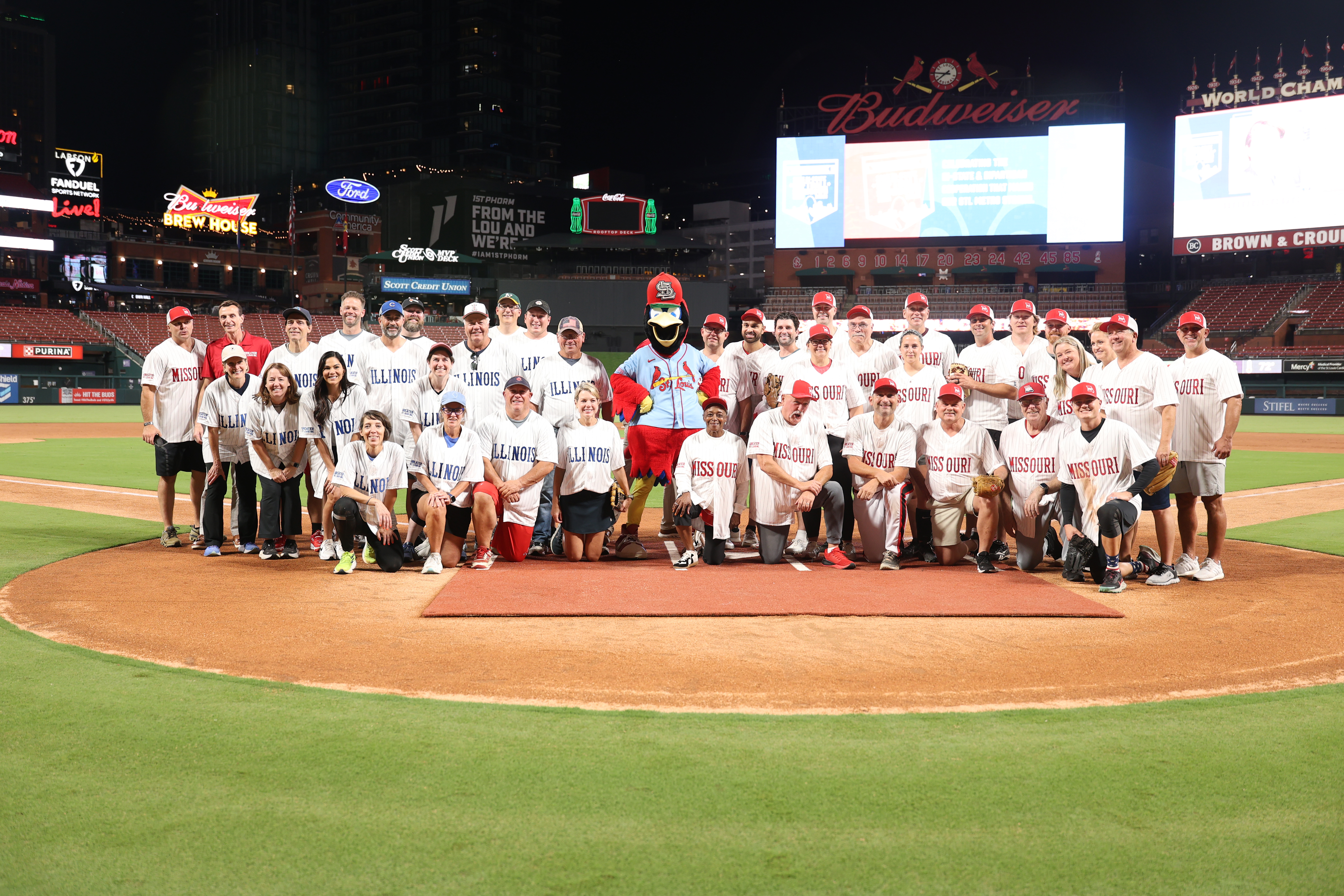At the Greater St. Louis, Inc. 2025 Bi-State Softball Showdown, MO and IL teams pose together on the field at Busch Stadium.