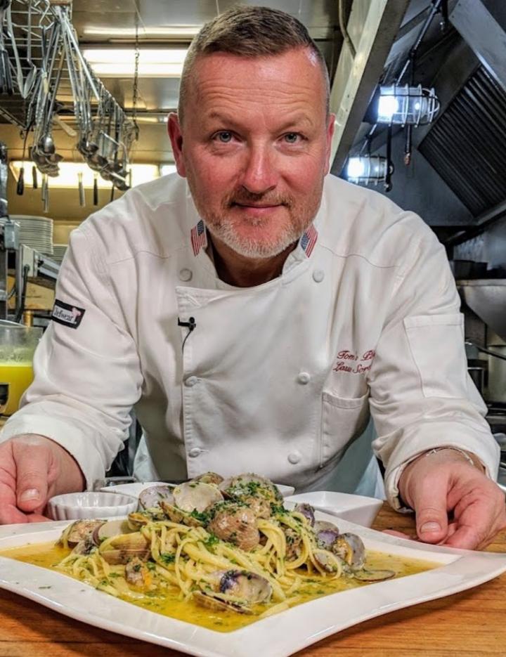 Photo of a chef holding a plate of pasta in a professional kitchen