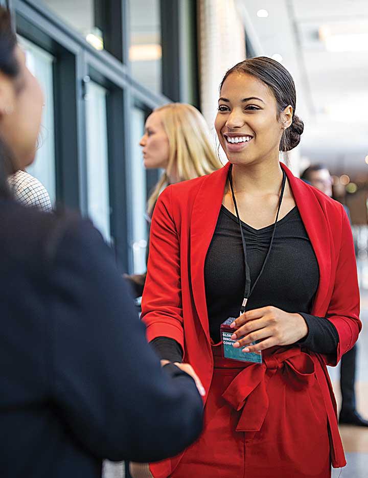 A woman of color in a red suit shaking hands with other people of color in a business setting