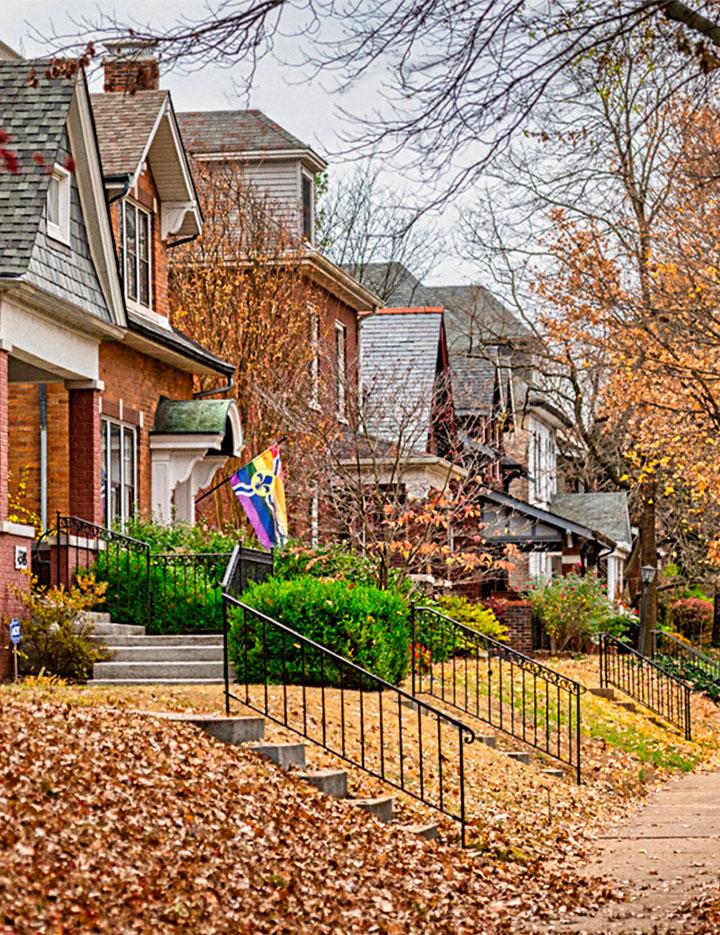 Brick homes during autumn, one flying a St. Louis Pride flag