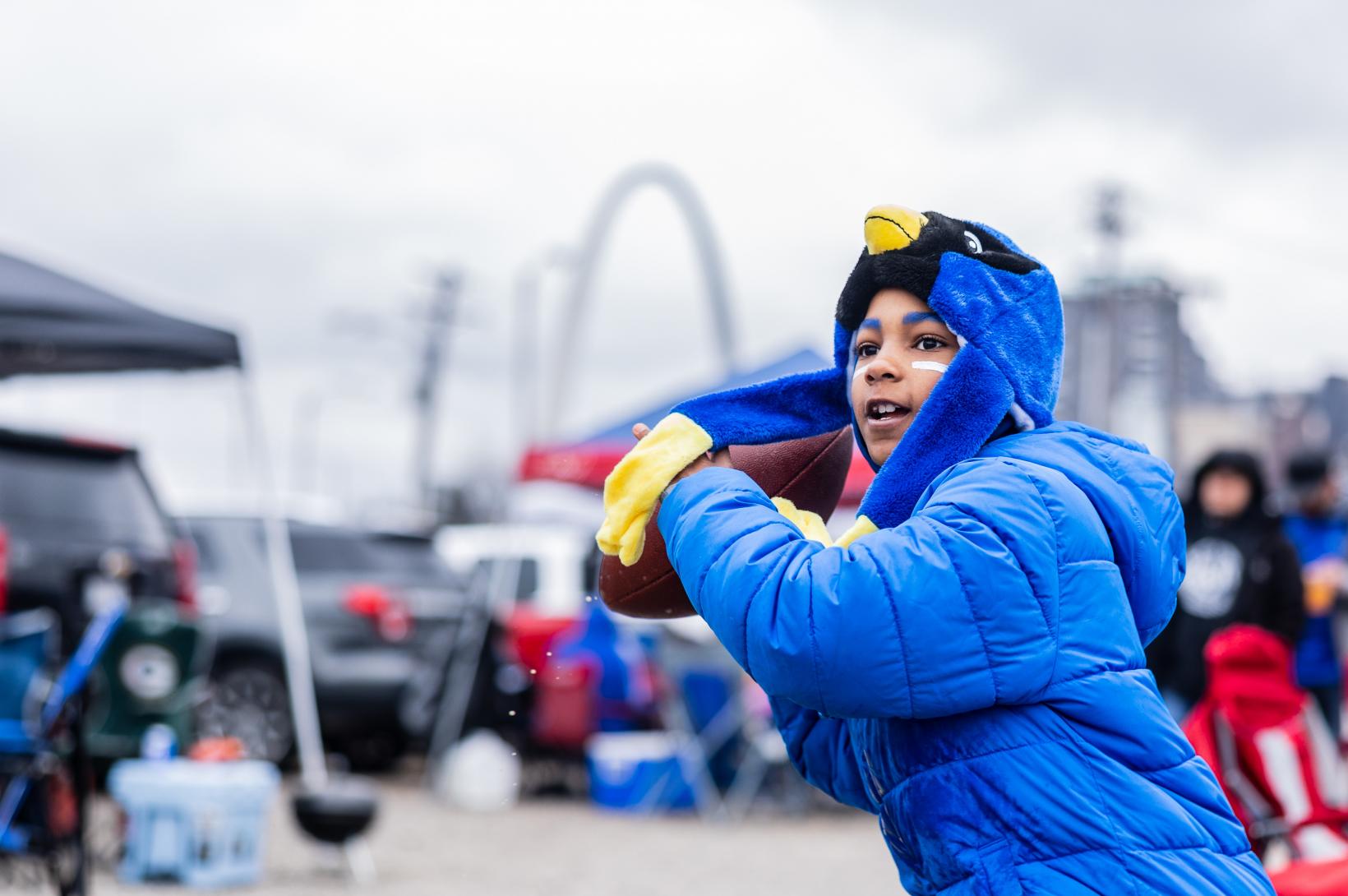 Young STL Battlehawks Fan in a Blue jacket throwing a football with the St. Louis Arch in the background before a Battlehawks Football Game