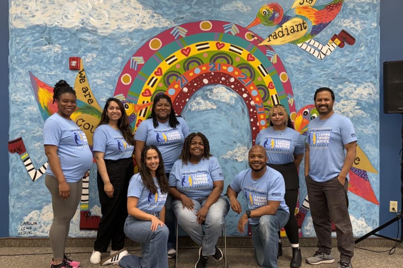 A group of the 19th Fellows Experience cohort poses in front of a painting of a rainbow at the Down Syndrome Association of St. Louis 