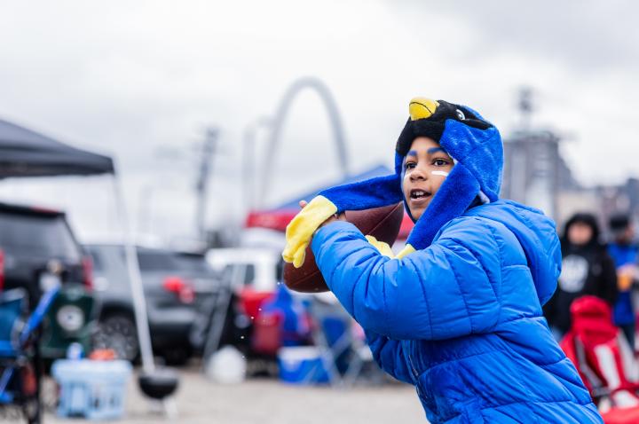 Young STL Battlehawks Fan in a Blue jacket throwing a football with the St. Louis Arch in the background before a Battlehawks Football Game