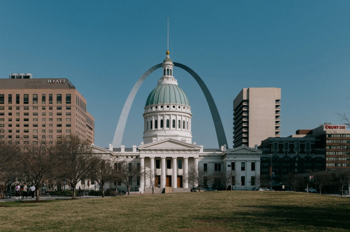 The image depicts the St. Louis cityscape with a prominent Old Courthouse in front, featuring a green dome and the Gateway Arch in the background.