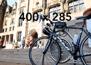 Road bicycle locked to a metal rack in front of stone steps and a historic building with arched windows, blurred pedestrians on the steps, and a large '400 x 285' placeholder text over the image.