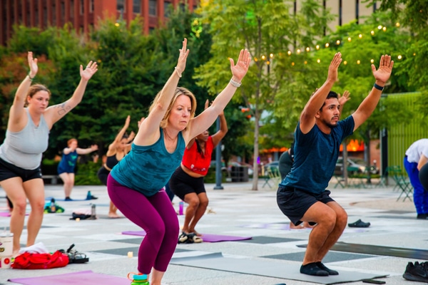 Long row of varied beer tap handles mounted above a stainless-steel drip tray, with wooden shelves of bottles and glassware on a brick back wall.
