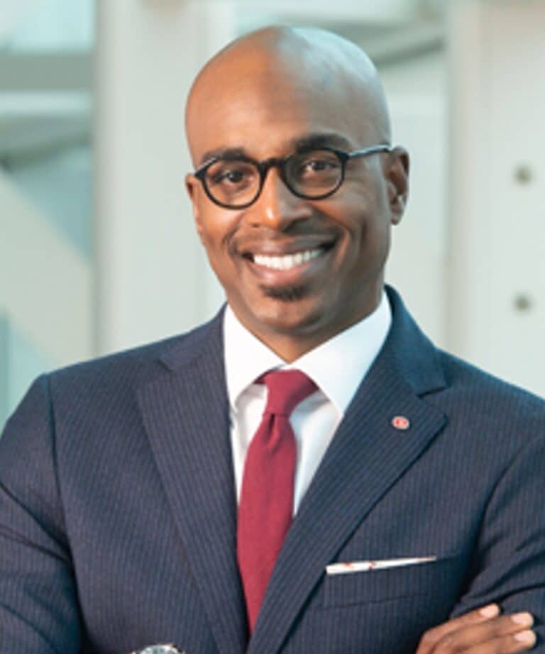 Smiling bald man in glasses wearing a navy pinstripe suit, white shirt and red tie with his arms crossed