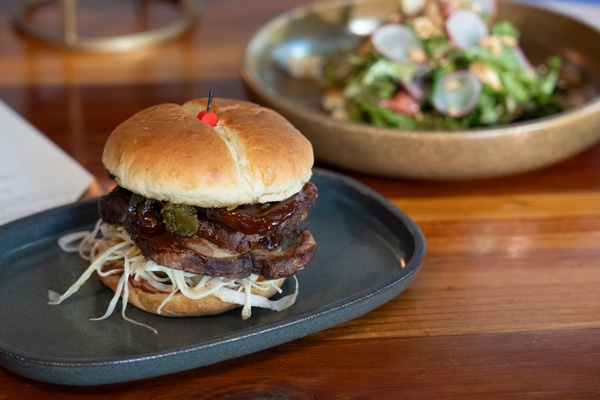 Neoclassical memorial building with tall rectangular columns, a carved dedication across the top, two flagpoles and stone soldier statues at the entrance, mirrored in a calm reflecting pool engraved with 'NAVY' and 'AIR FORCE', with a clear blue sky and city buildings in the background.