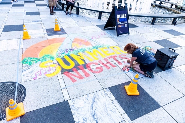 Stainless-steel Gateway Arch towering over a broad green park with a circular fountain and walkways, framing the downtown St. Louis skyline under a bright blue sky.
