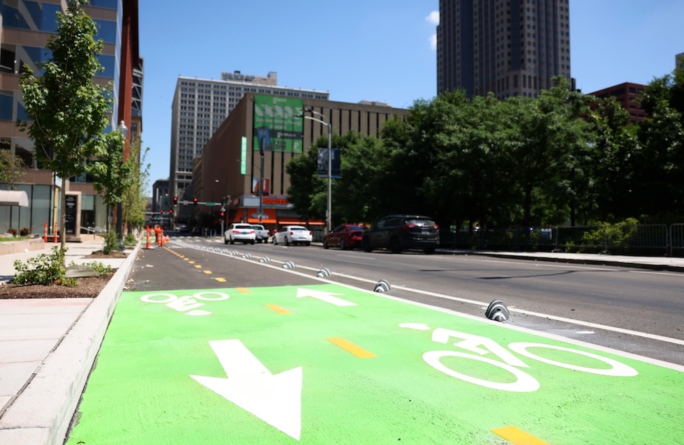 Green protected bike lane with white bike symbols and arrows separated from traffic by short posts on a city street.