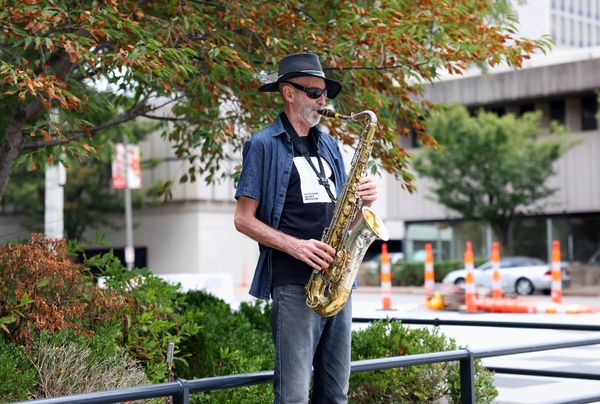 Red brick Victorian-style house with a rounded turret and arched porch behind a low stone wall, an American flag and flowering shrubs at the entrance under an overcast sky.