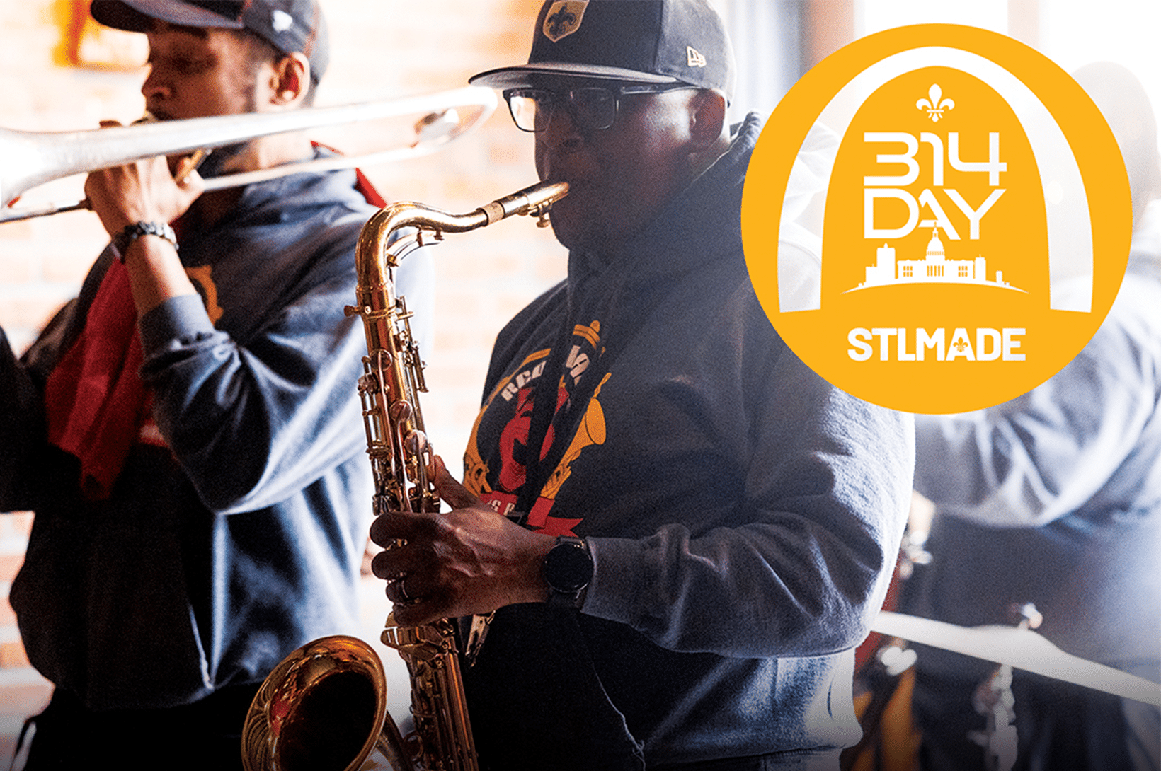 Saxophonist in cap and glasses plays with a trombonist blurred behind him and a yellow 314 Day STLMADE logo to the right.