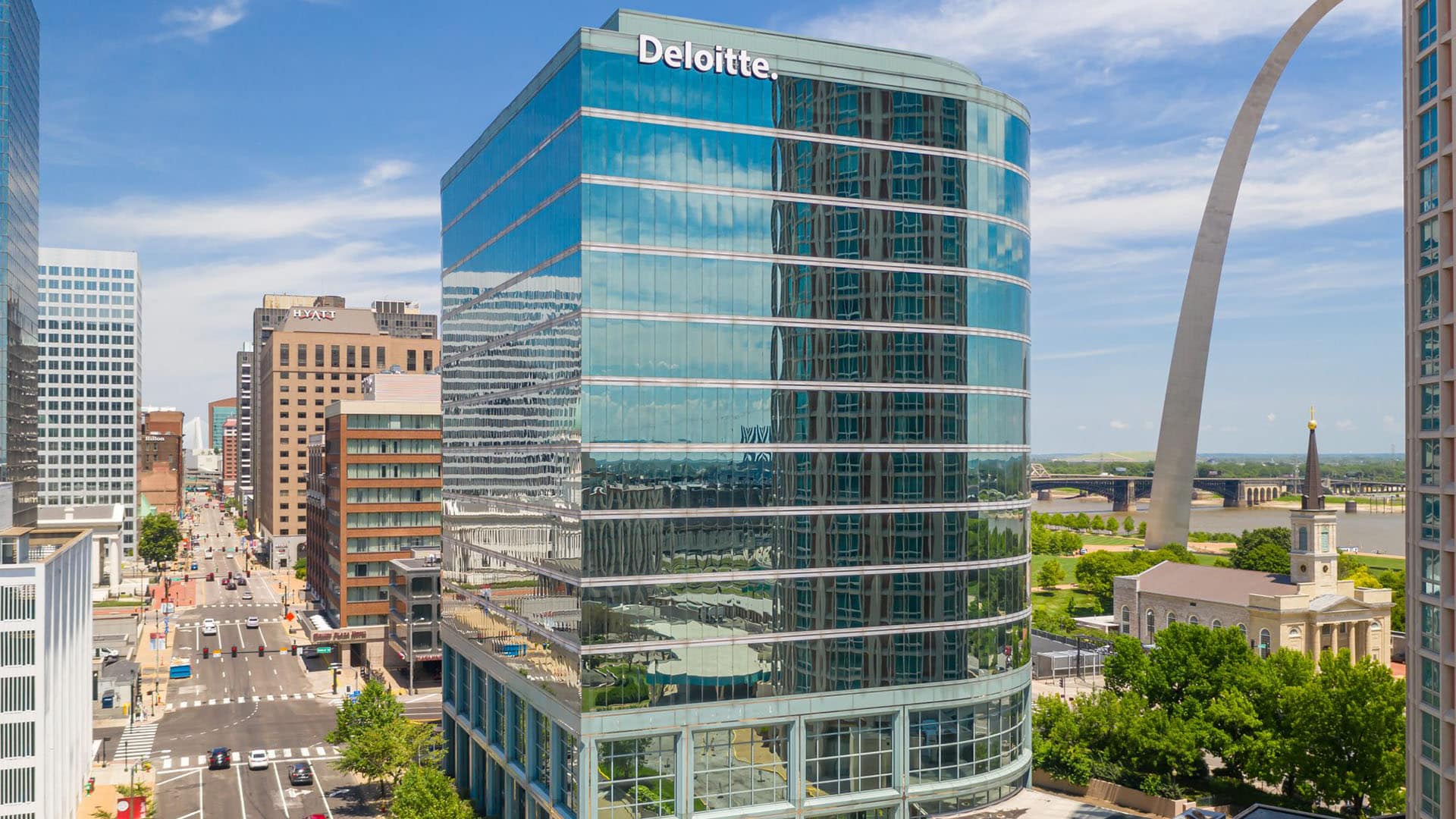 Deloitte Building Exterior Curved glass Deloitte office tower reflecting nearby buildings, with the Gateway Arch and a riverside church to the right