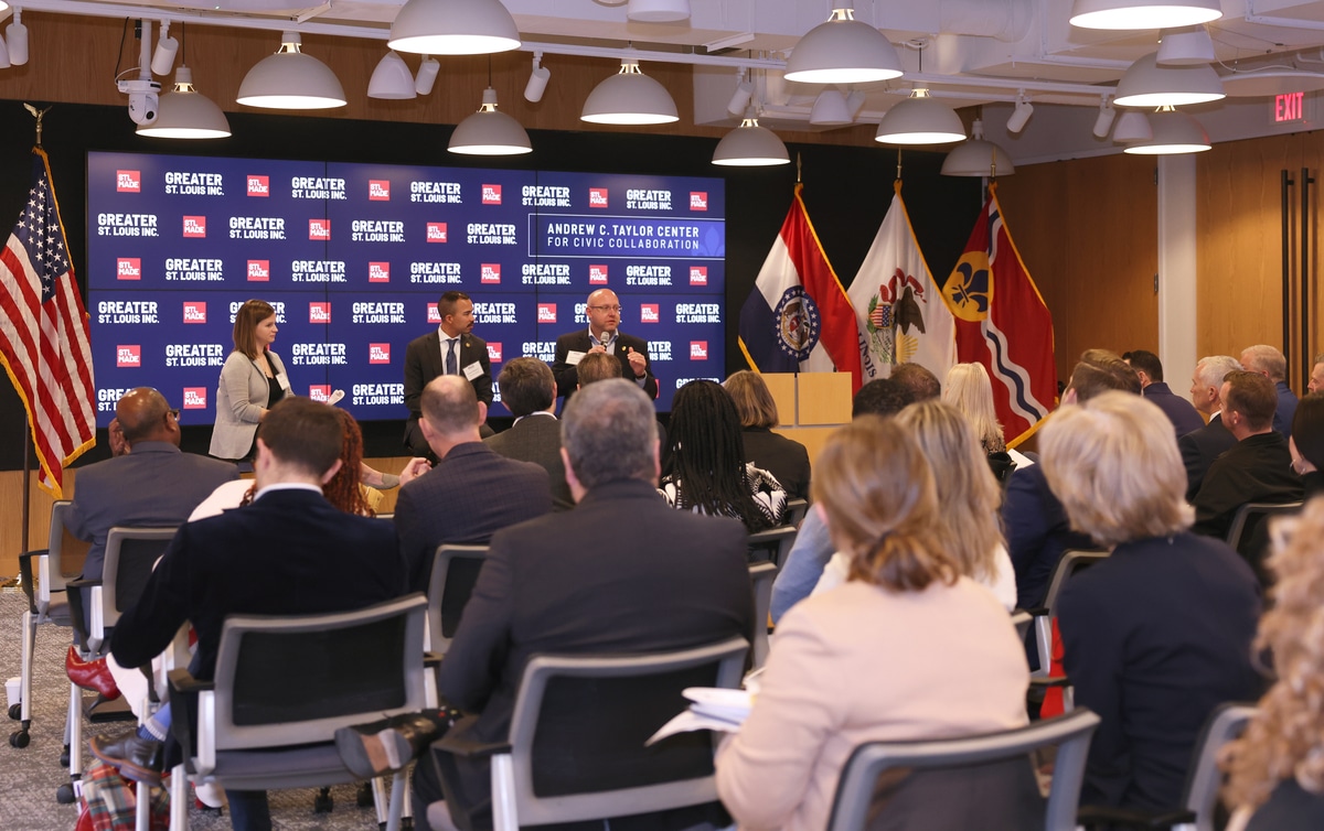 Panel discussion with three speakers, audience facing a large screen of Greater St. Louis logos and flags.