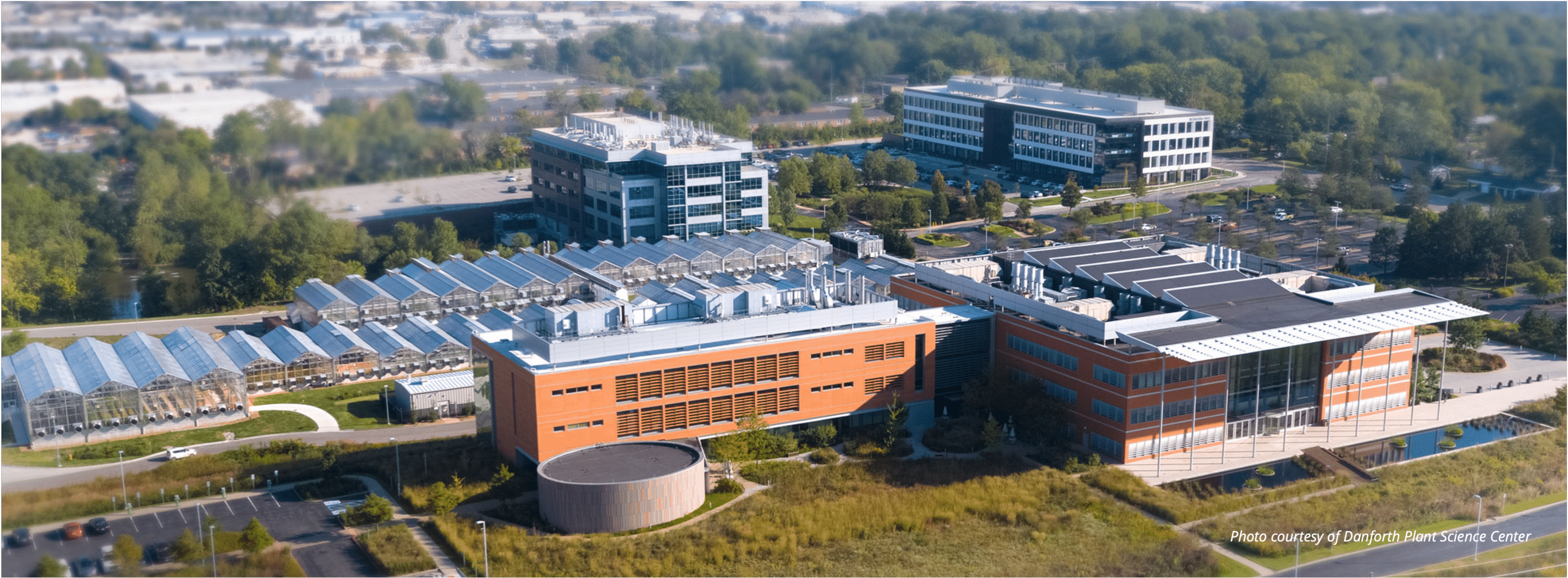 Aerial view of Danforth Plant Science Center: glass greenhouses alongside modern brick research buildings and ponds.