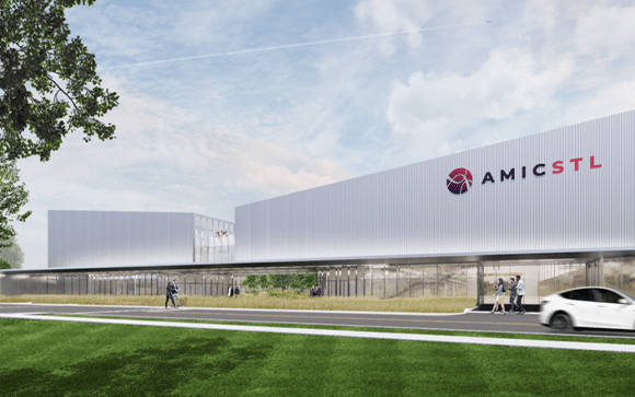 Modern silver-clad building with large AMICSTL logo, glazed ground level, pedestrians on the sidewalk and a car driving by.