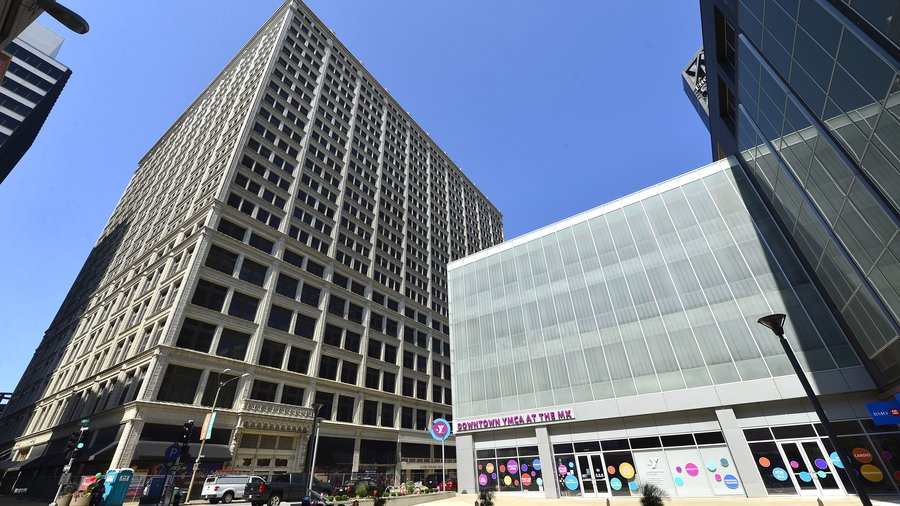 Low-angle view of a tall grid-patterned historic office building next to a modern glass-front YMCA.