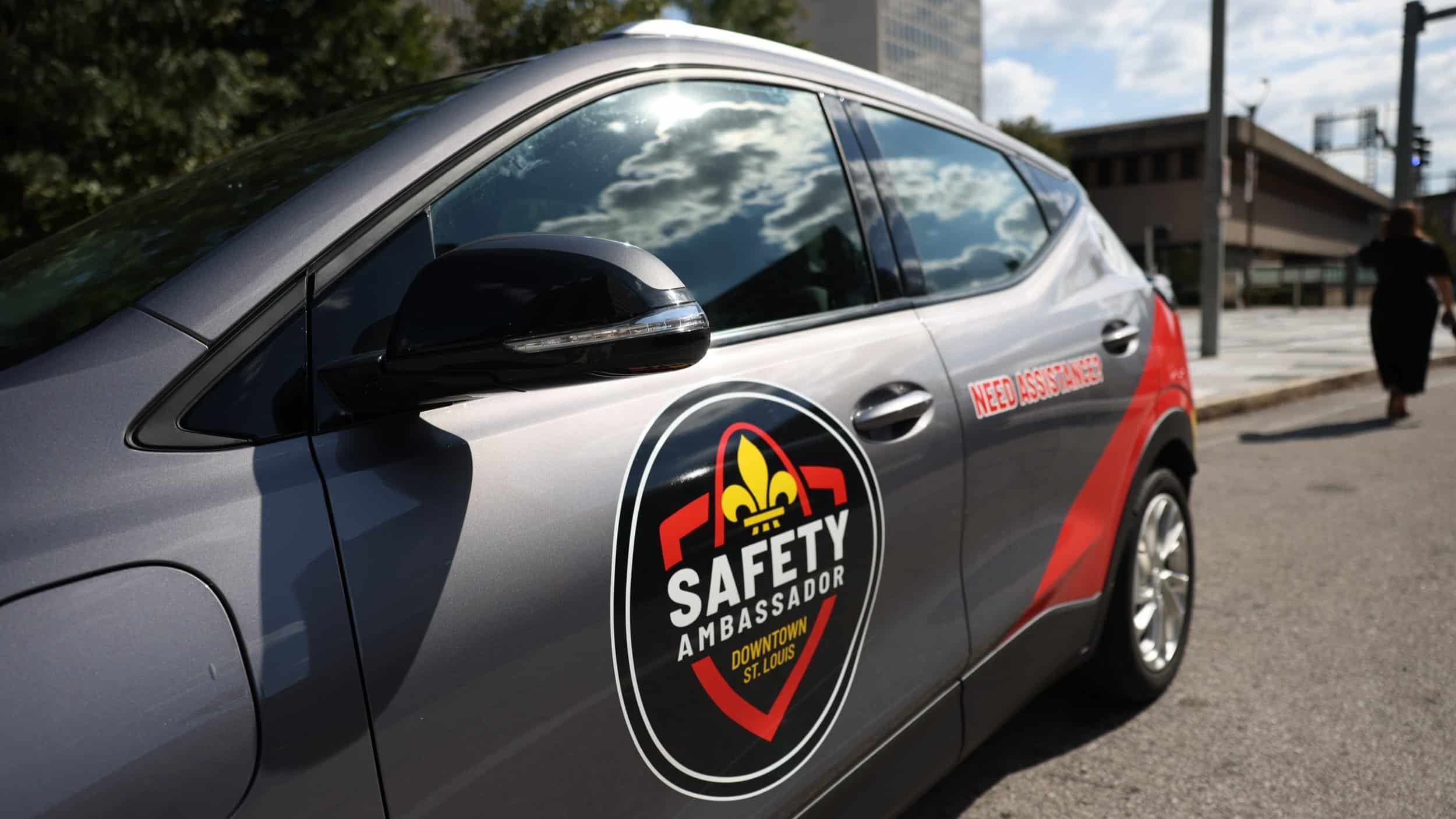 safetyambassadorassets6.jpg Gray SUV door with Safety Ambassador Downtown St. Louis logo and Need Assistance text, clouds reflected in the window.