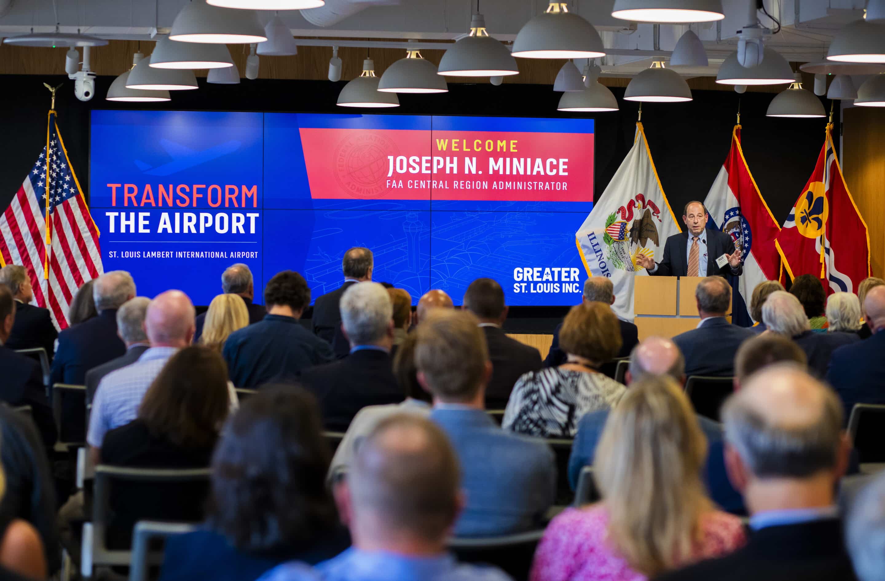 Man at podium speaking to seated audience in front of screens reading Transform the Airport and a welcome FAA banner