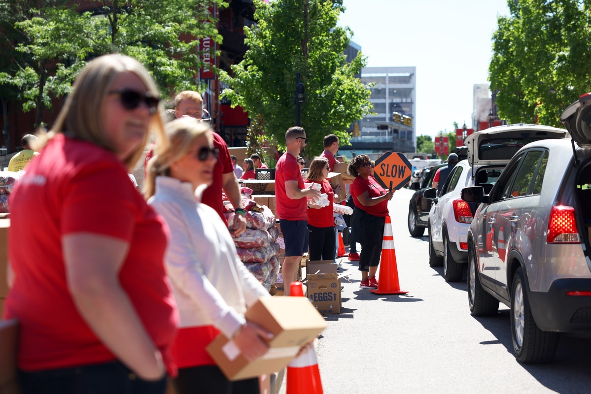 Purina Cares Day BPV 10-1200×800-5b2df79 Volunteers in red shirts hand boxes to drivers at a street-side food pick-up while a woman holds a SLOW sign.
