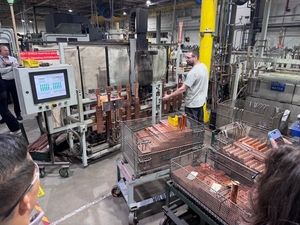 Factory workers operating electroplating tanks with copper parts in wire baskets, control panel and carts of finished copper pieces nearby