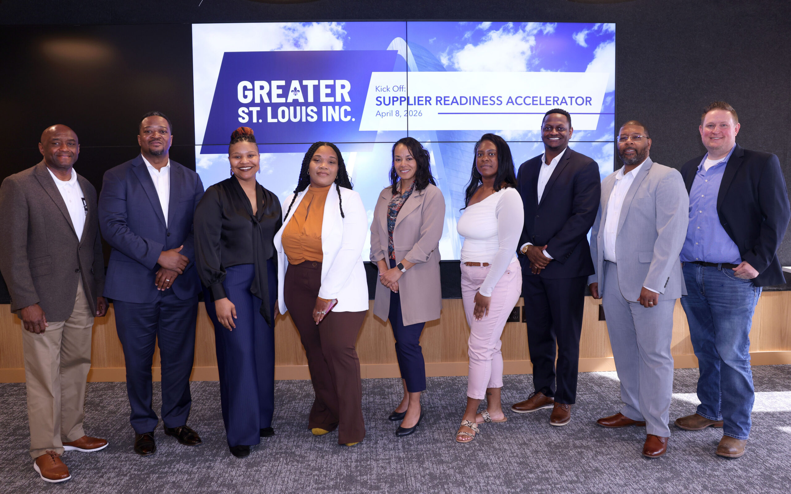 Nine professionally dressed people pose in front of a Greater St. Louis Inc. Supplier Readiness Accelerator kickoff screen