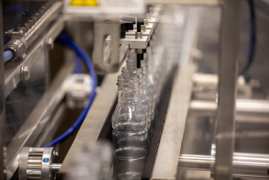 Empty clear plastic bottles moving along a stainless steel conveyor in an automated bottling machine