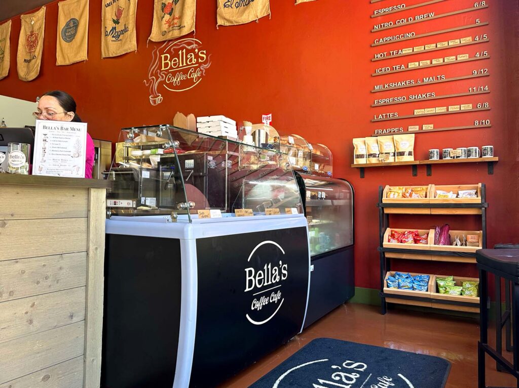Interior of Bella's Coffee Cafe with orange walls, a display counter, menu board, and snack shelves