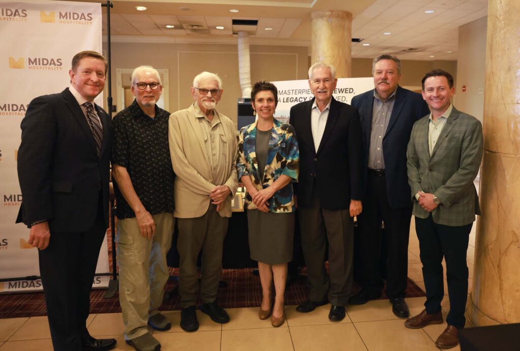 Seven people pose together at an event in front of a Midas Hospitality banner