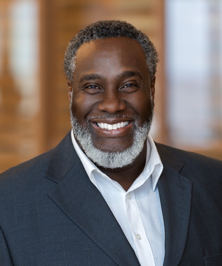 Smiling man with gray beard wearing a dark gray blazer and white shirt in a professional headshot