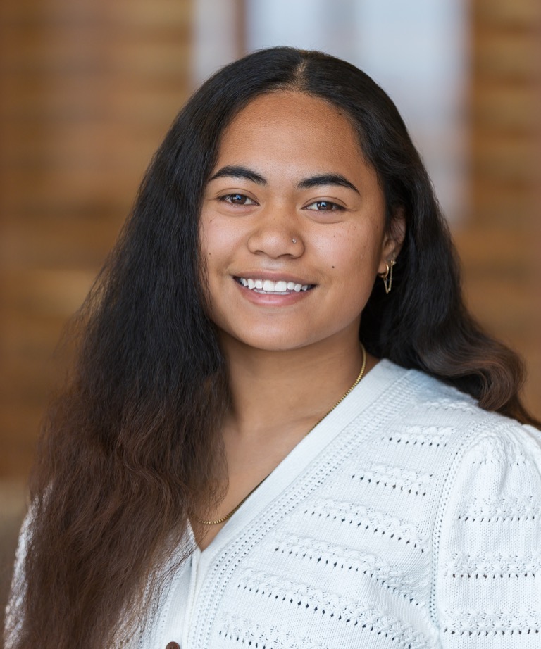 Smiling young woman with long dark hair wearing a white knit cardigan and gold necklace