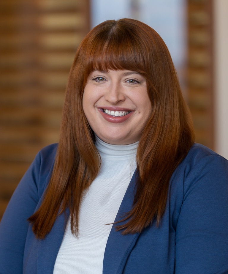 Smiling woman with long red hair wearing a white turtleneck and blue blazer in a professional headshot