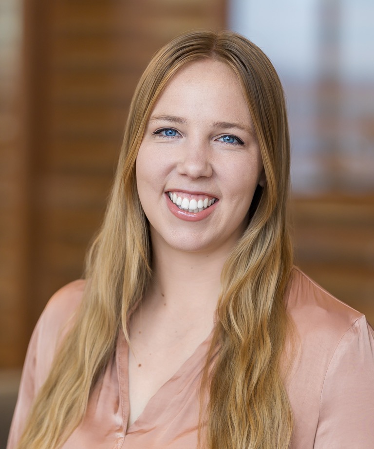 Smiling woman with long blonde hair wearing a pink blouse in a professional headshot