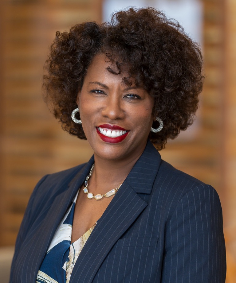 Smiling woman with curly hair in a navy pinstripe blazer and pearl necklace, professional headshot