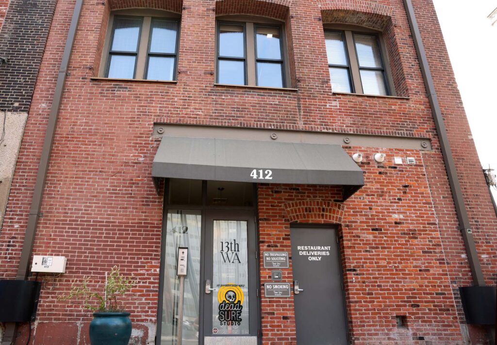 Red brick building entrance numbered 412 with gray awning, glass door for 13th WA studio, and delivery-only side door