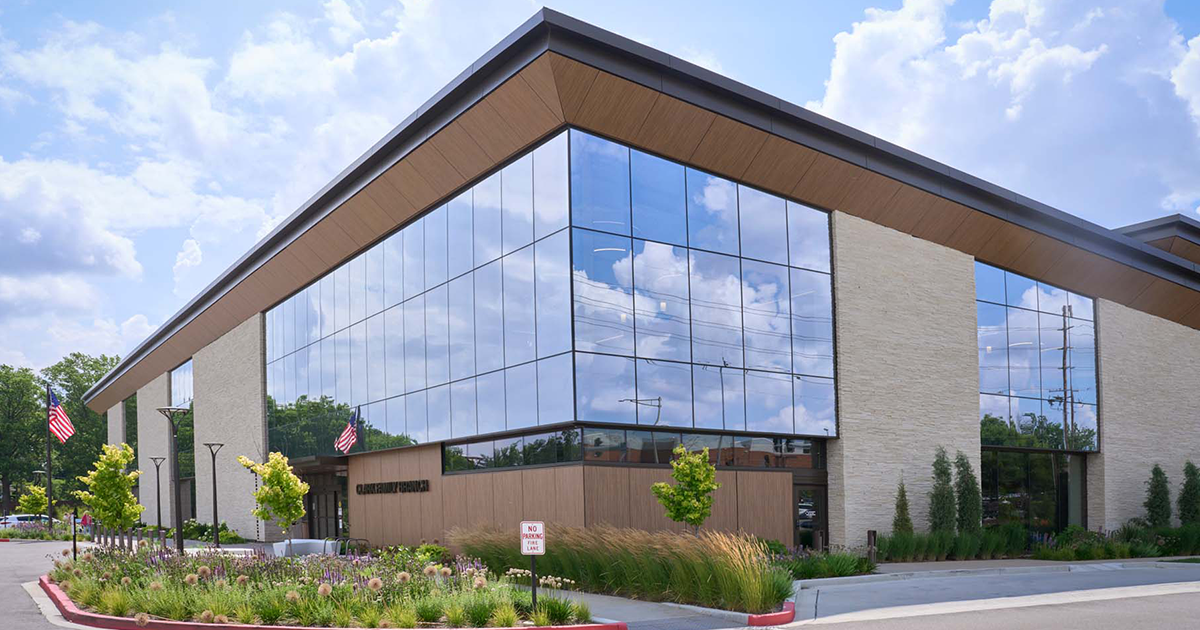 Modern building with large glass facade, stone walls, American flags, and landscaped gardens under a blue sky