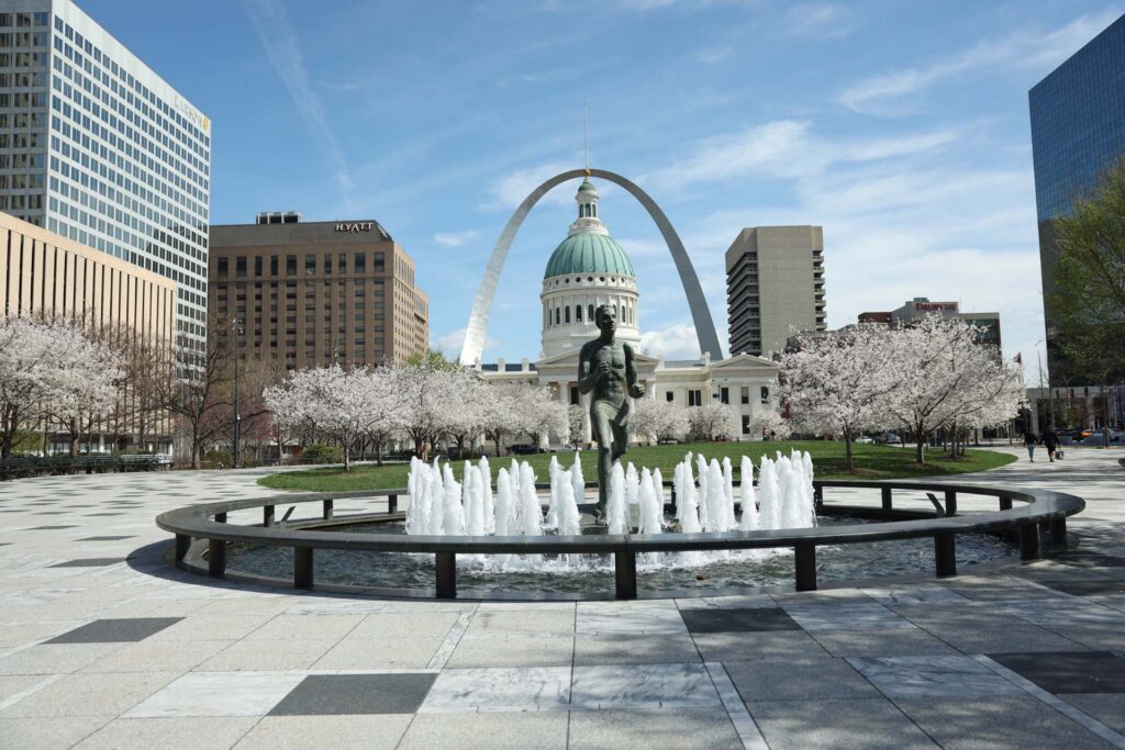 Runner statue in a fountain framed by cherry blossoms, the Old Courthouse, and Gateway Arch in St. Louis