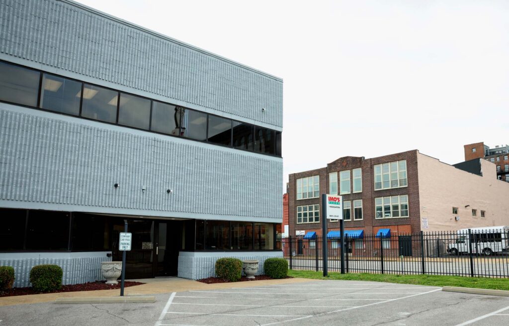 Imo's Pizza headquarters, a brick building beside a gray office building and parking lot in an urban setting