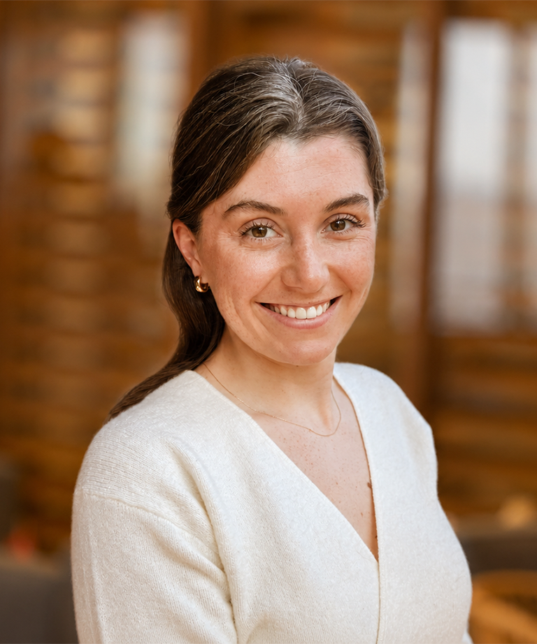 Smiling woman with dark hair in a cream sweater against a warm blurred background