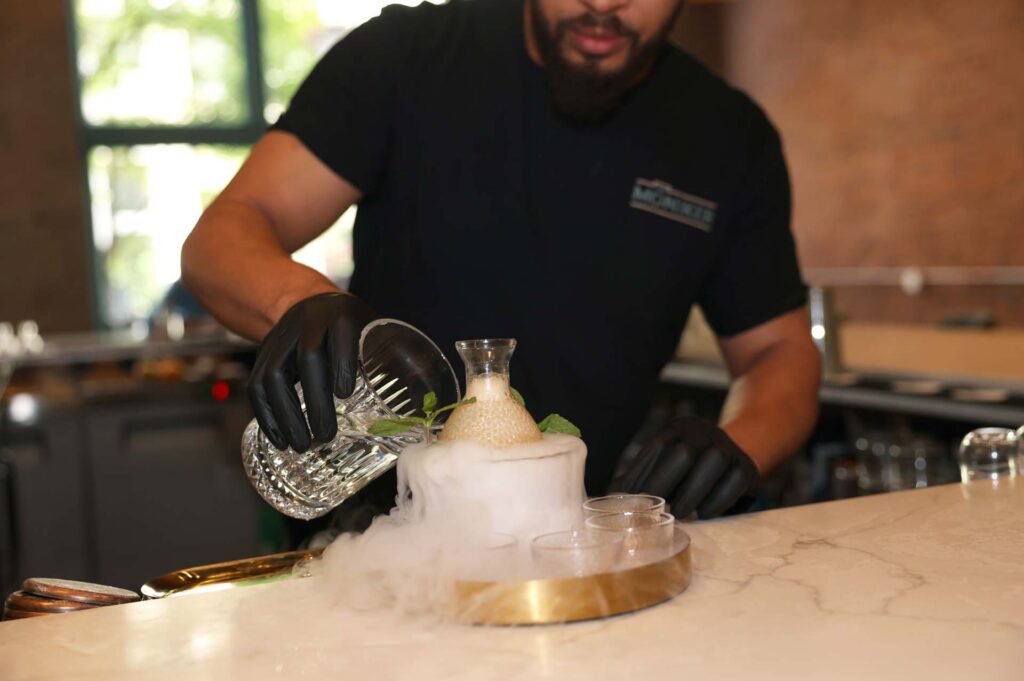 Bartender in black gloves prepares a smoking dry-ice cocktail with mint garnish at a marble bar