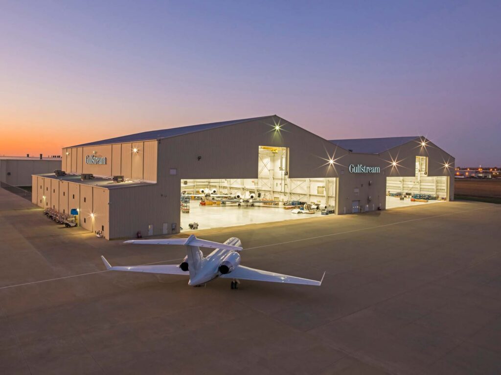 Gulfstream hangars lit at dusk with a business jet parked on the tarmac and more aircraft inside