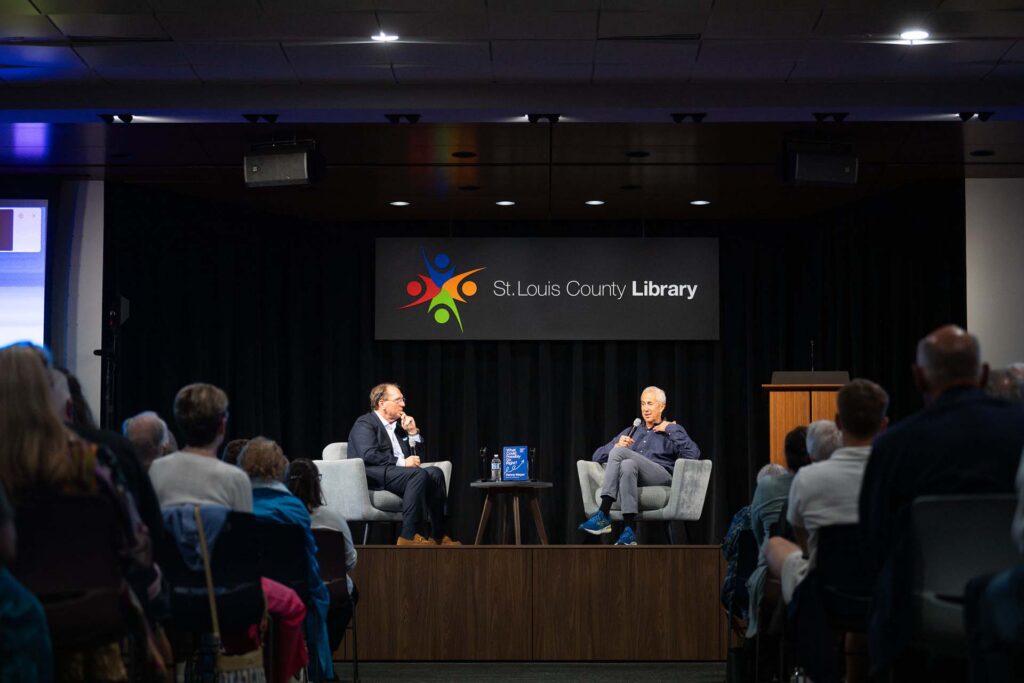 Two men in armchairs hold an on-stage conversation before an audience at a St. Louis County Library author event