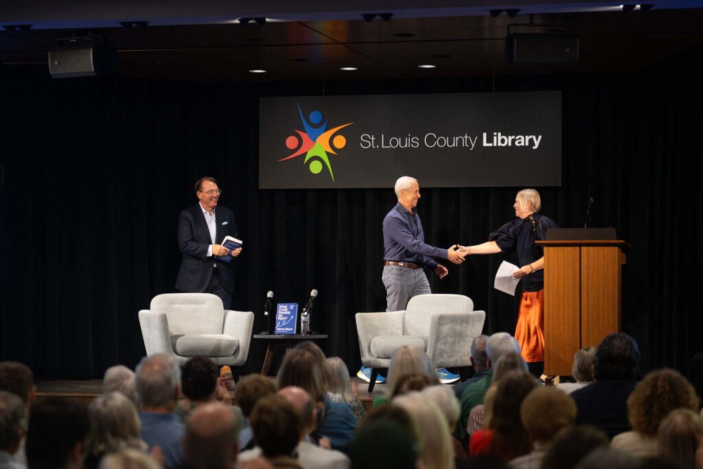 Speaker shakes hands with a host on stage at a St. Louis County Library event before a seated audience