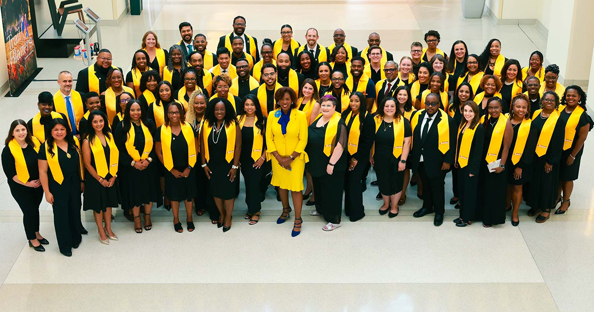 Large group in black attire wearing yellow graduation stoles, posing together indoors