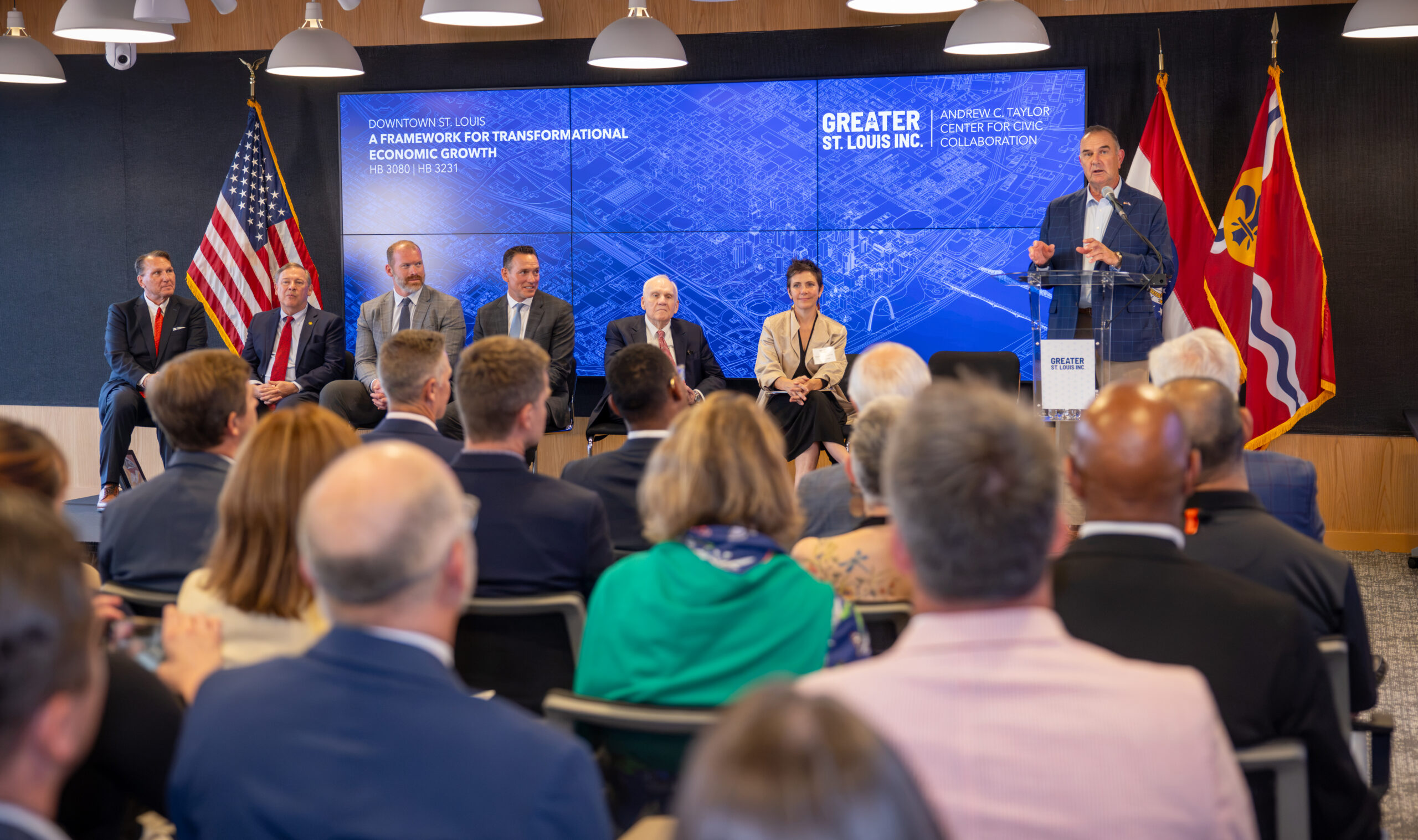 A man speaks at a podium before an audience, with panelists seated beside a screen reading "A Framework for Transformational Economic Growth