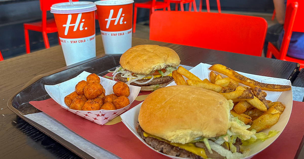 Tray with two cheeseburgers, seasoned fries, fried cheese curds, and two drink cups labeled "Hi