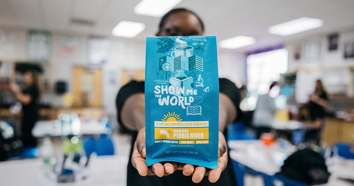 Person holding out a blue "Show Me the World" Costa Rica Pirris River single origin coffee bag that supports local education