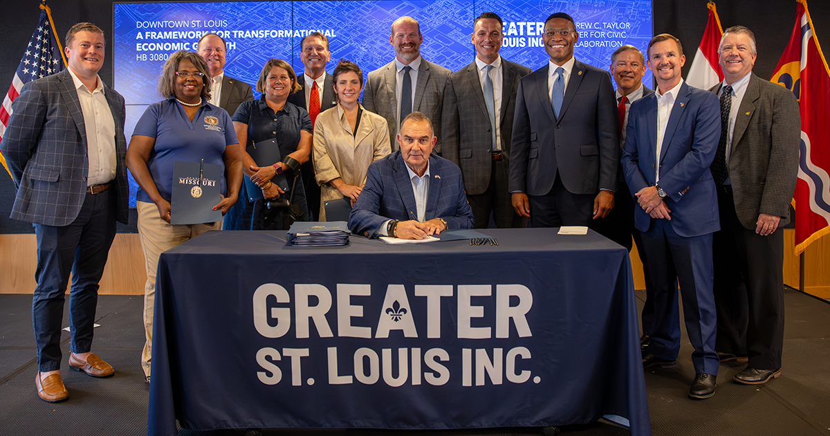 A man signs HB 3080 at a Greater St. Louis Inc. table as officials stand behind him for a bill signing ceremony