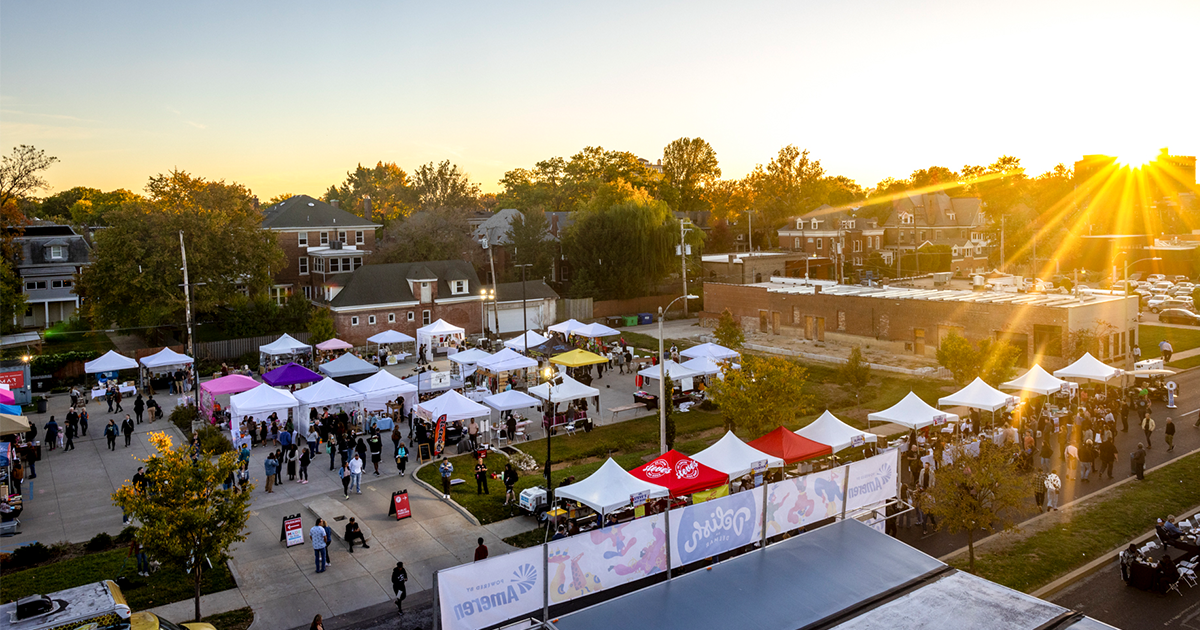 Aerial view of an outdoor festival with rows of vendor tents and crowds in a residential neighborhood at sunset